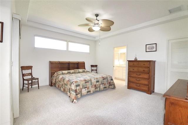 carpeted bedroom featuring a raised ceiling, ensuite bathroom, multiple windows, and ceiling fan