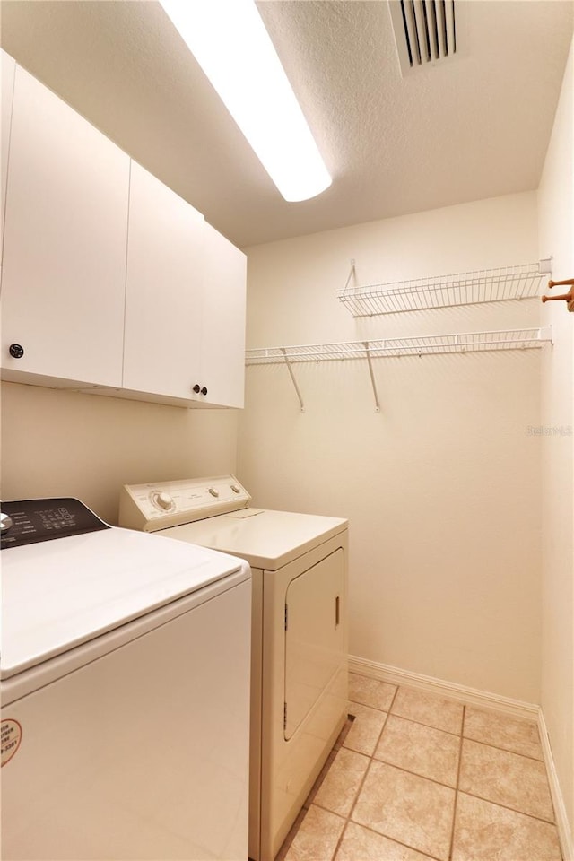 clothes washing area featuring cabinets, independent washer and dryer, and light tile floors