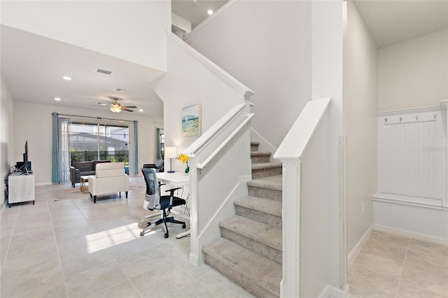 stairway featuring ceiling fan, light tile floors, and a towering ceiling