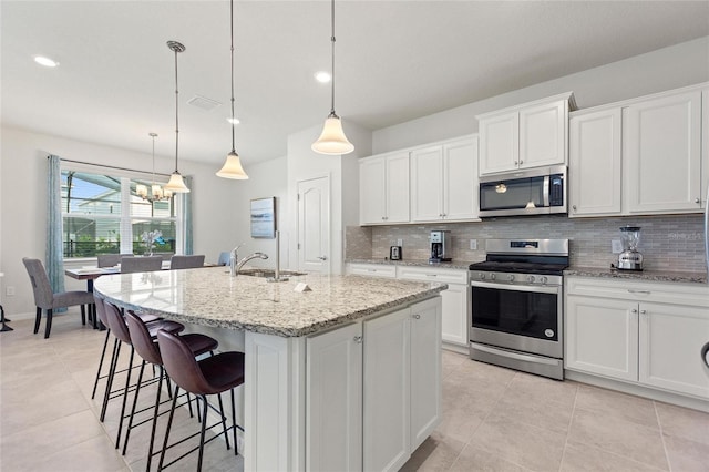 kitchen with a chandelier, pendant lighting, stainless steel appliances, white cabinetry, and light stone counters