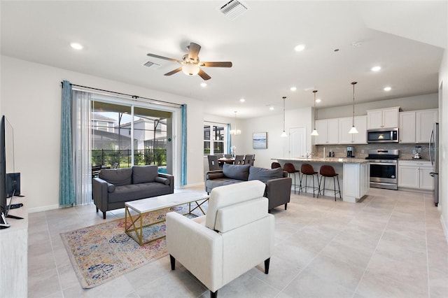 tiled living room featuring ceiling fan with notable chandelier