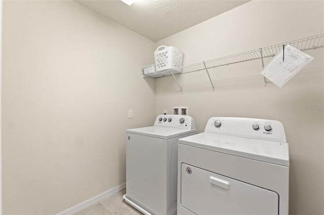 clothes washing area with washer and clothes dryer, a textured ceiling, and light tile flooring