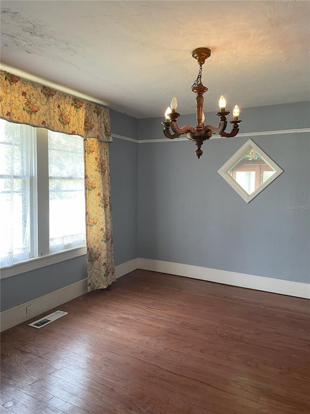 spare room with an inviting chandelier and dark wood-type flooring