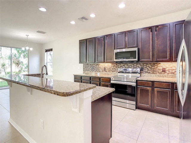 kitchen featuring decorative light fixtures, a kitchen island with sink, stainless steel appliances, and a breakfast bar area