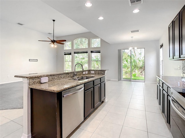 kitchen with light stone countertops, appliances with stainless steel finishes, sink, a center island with sink, and decorative light fixtures