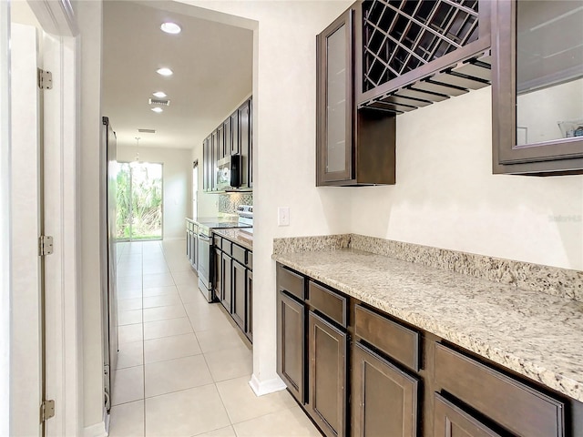 kitchen with light stone countertops, light tile patterned floors, dark brown cabinetry, and stainless steel appliances