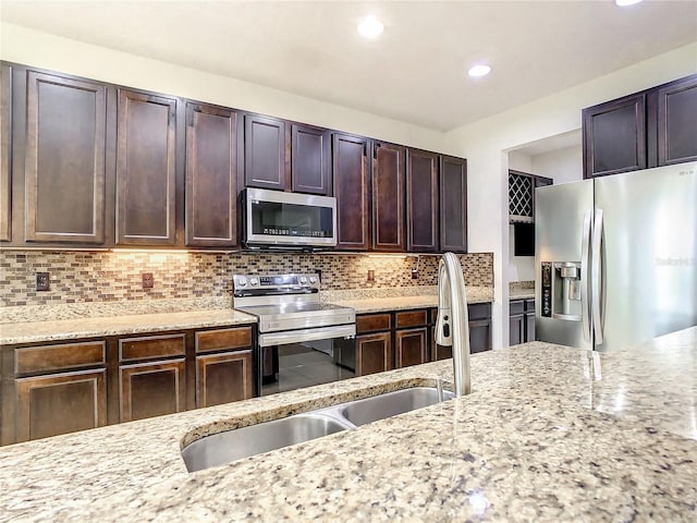 kitchen with sink, decorative backsplash, dark brown cabinets, light stone counters, and stainless steel appliances