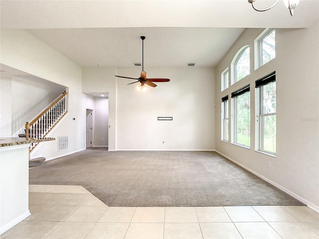 unfurnished living room featuring a towering ceiling, light colored carpet, and ceiling fan with notable chandelier