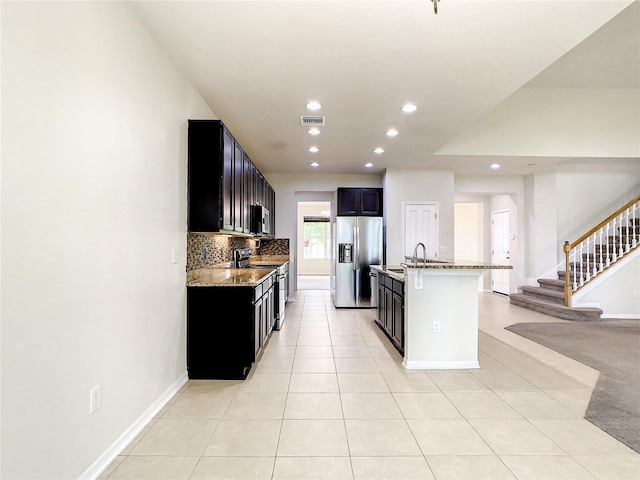 kitchen with light tile patterned floors, light stone counters, an island with sink, a kitchen bar, and stainless steel appliances