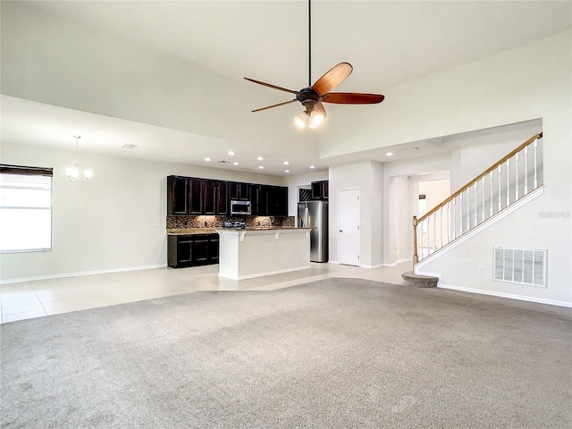 unfurnished living room with ceiling fan with notable chandelier, light colored carpet, and a high ceiling