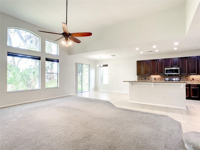 unfurnished living room with a towering ceiling, light tile patterned floors, and ceiling fan with notable chandelier