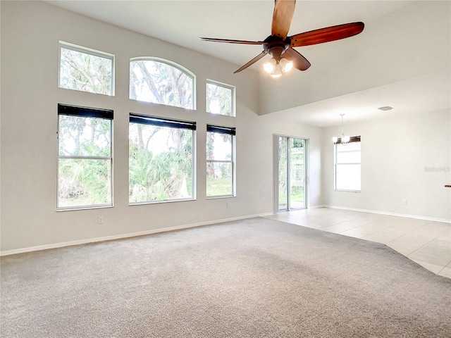 carpeted spare room featuring a high ceiling and ceiling fan with notable chandelier