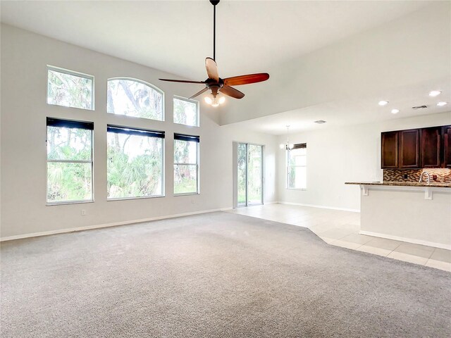 unfurnished living room with ceiling fan with notable chandelier, a healthy amount of sunlight, and light colored carpet