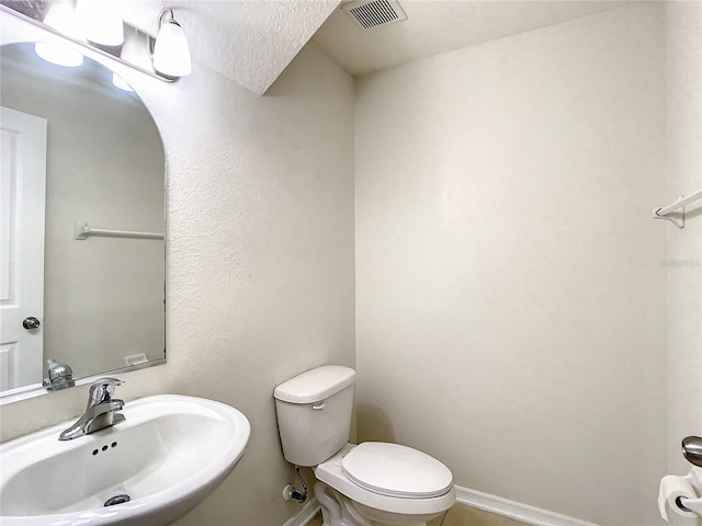 bathroom with a textured ceiling, toilet, and sink