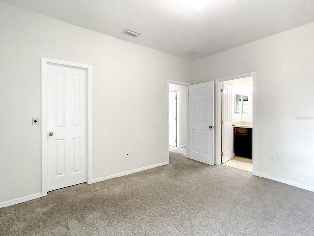 unfurnished bedroom with ensuite bath, a closet, and light colored carpet