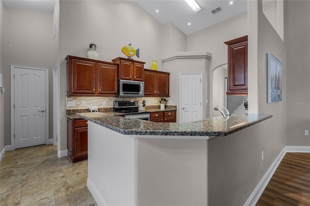 10120 Lakeshore Dr, Clermont, FL 34711 - kitchen featuring stainless steel appliances, high vaulted ceiling, decorative backsplash, a peninsula, and dark stone countertops