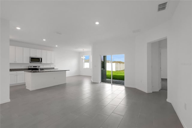 kitchen with stainless steel appliances, light tile patterned floors, a kitchen island with sink, white cabinetry, and dark stone countertops