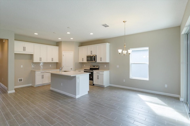 kitchen with a kitchen island with sink, pendant lighting, a chandelier, stainless steel appliances, and white cabinetry