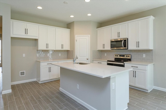 kitchen featuring a kitchen island with sink, appliances with stainless steel finishes, sink, white cabinets, and tasteful backsplash