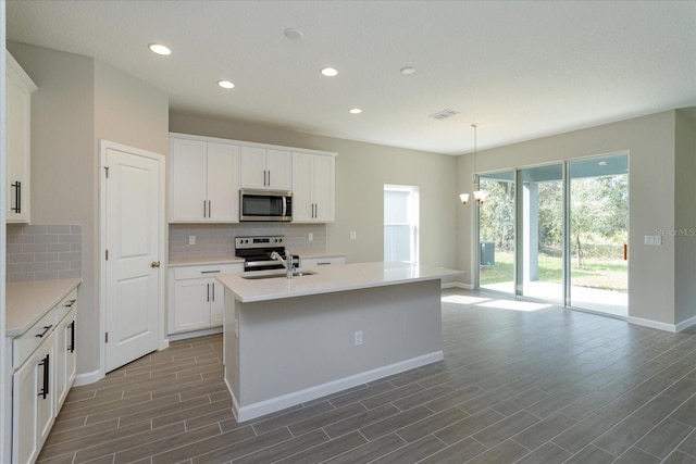 kitchen with a chandelier, a center island with sink, appliances with stainless steel finishes, white cabinetry, and hanging light fixtures