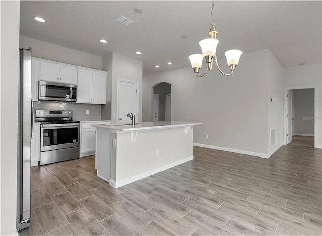 kitchen featuring hanging light fixtures, an inviting chandelier, appliances with stainless steel finishes, an island with sink, and white cabinets