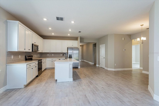 kitchen with a chandelier, a center island with sink, appliances with stainless steel finishes, white cabinets, and light wood-type flooring