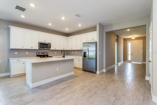 kitchen with a center island with sink, stainless steel appliances, white cabinetry, and sink