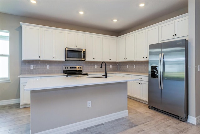 kitchen with a center island with sink, stainless steel appliances, a healthy amount of sunlight, and white cabinetry