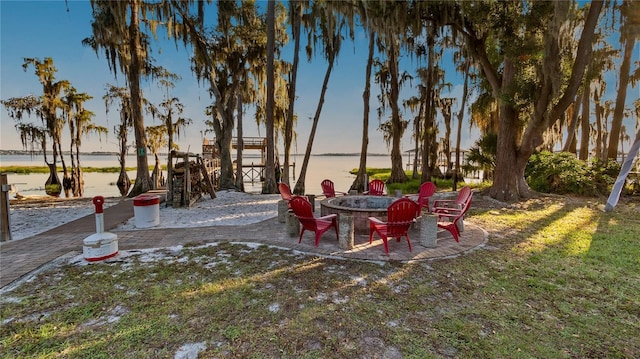 yard at dusk featuring a patio, a water view, and a fire pit