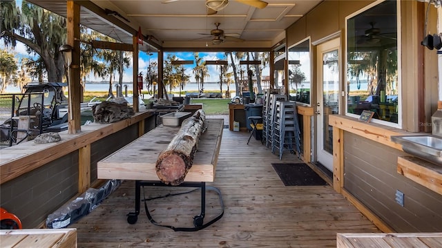 wooden deck with a water view, ceiling fan, and a bar