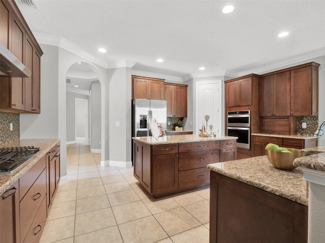 kitchen with appliances with stainless steel finishes, arched walkways, ornamental molding, and light tile patterned floors