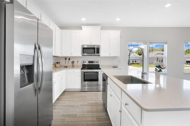 kitchen featuring a kitchen island, appliances with stainless steel finishes, white cabinetry, sink, and light stone counters