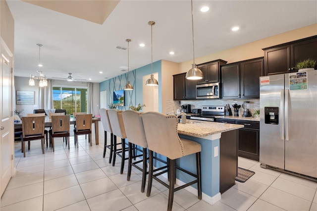 kitchen featuring a center island with sink, ceiling fan, appliances with stainless steel finishes, a kitchen breakfast bar, and hanging light fixtures