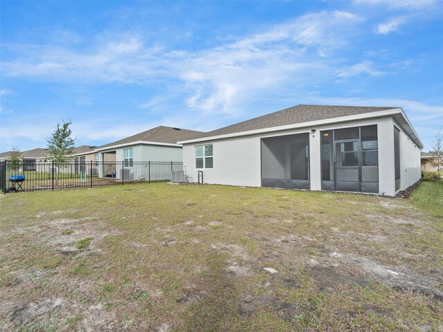 rear view of property with a sunroom, central AC, and a lawn