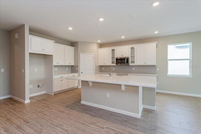 kitchen with sink, white cabinetry, tasteful backsplash, and an island with sink