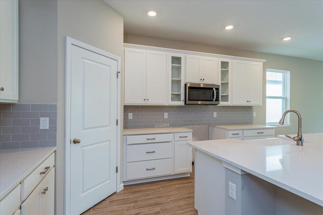 kitchen with white cabinets, glass insert cabinets, stainless steel microwave, light countertops, and a sink