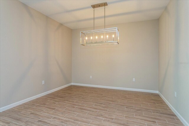 empty room featuring an inviting chandelier and light hardwood / wood-style flooring