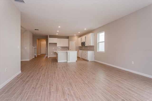 kitchen with stainless steel microwave, white cabinetry, open floor plan, light countertops, and an island with sink