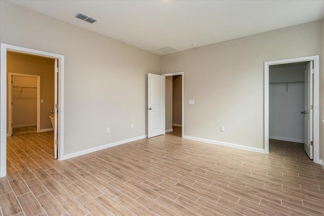 unfurnished bedroom featuring a closet, a spacious closet, and light hardwood / wood-style floors