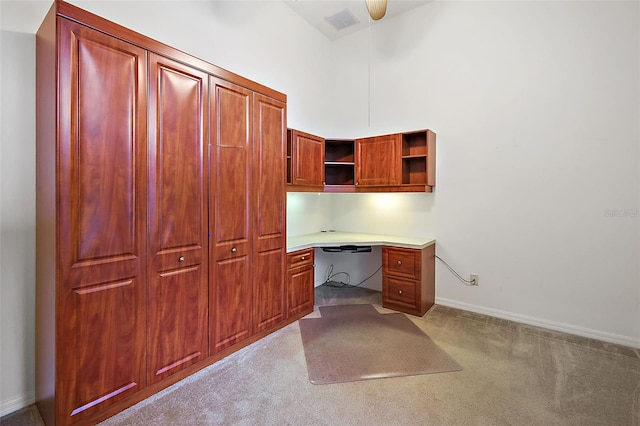 unfurnished office featuring light carpet, a towering ceiling, and built in desk