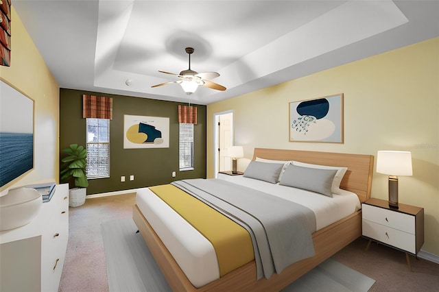 bedroom with a raised ceiling, ceiling fan, and carpet flooring