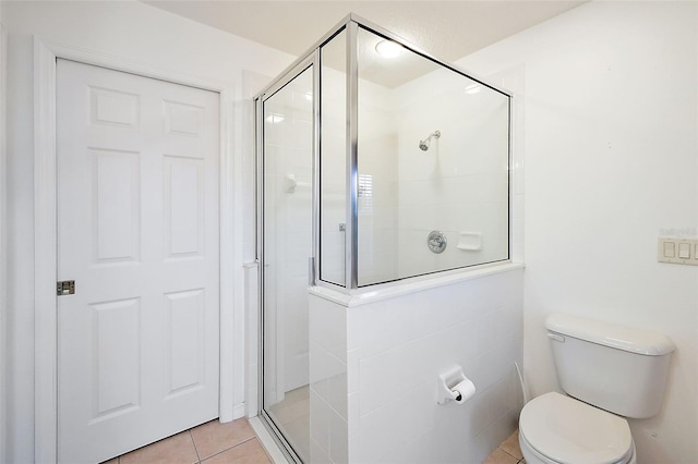 bathroom with tile patterned floors, toilet, and a shower with door