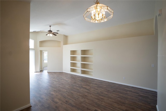 empty room with dark wood-type flooring, lofted ceiling, ceiling fan with notable chandelier, and built in features