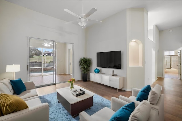 living room featuring a high ceiling, light wood-type flooring, and ceiling fan