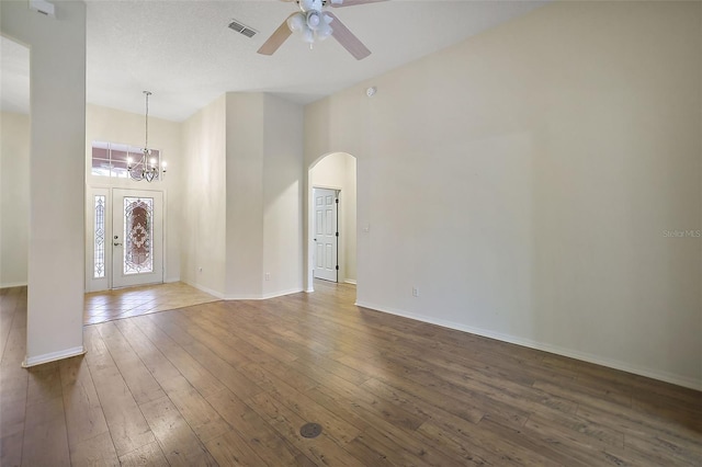 foyer entrance with ceiling fan with notable chandelier, a towering ceiling, and dark wood-type flooring