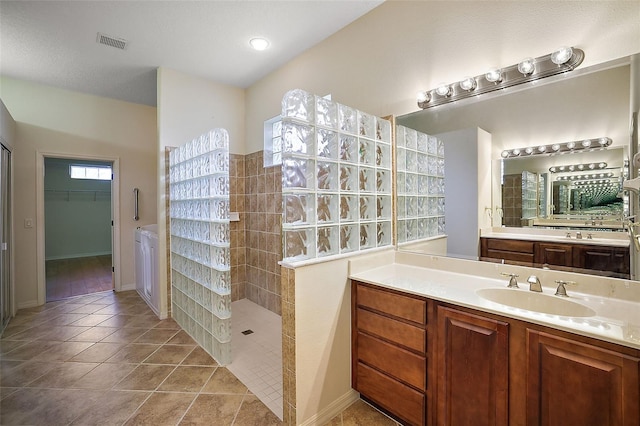 bathroom featuring tile patterned flooring, vanity, a tile shower, and a textured ceiling