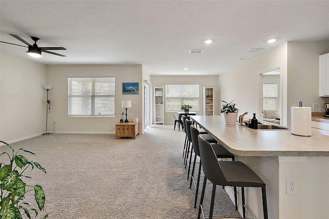 kitchen featuring white cabinets, a textured ceiling, light carpet, a breakfast bar area, and sink