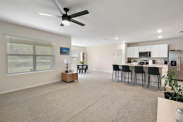 kitchen featuring stainless steel appliances, white cabinetry, a kitchen breakfast bar, light colored carpet, and ceiling fan