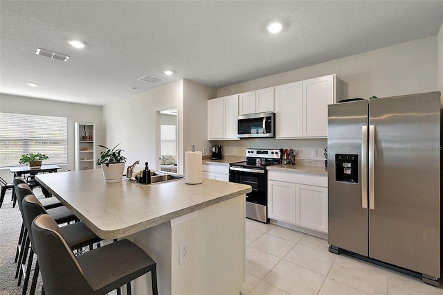 kitchen with stainless steel appliances, sink, a textured ceiling, an island with sink, and white cabinets