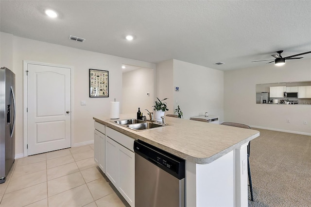 kitchen with sink, appliances with stainless steel finishes, an island with sink, white cabinets, and light colored carpet